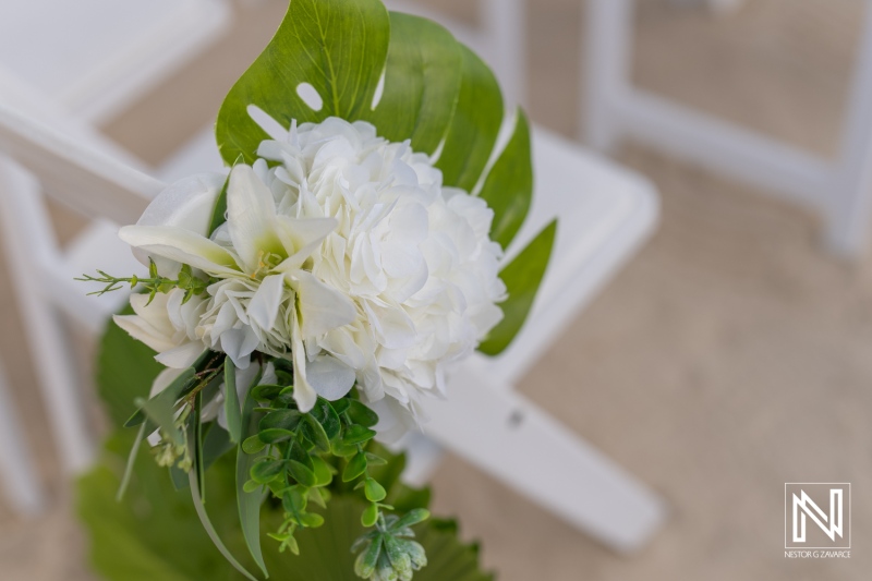 Elegant white floral arrangement with greenery placed on a white chair at a serene outdoor wedding setting