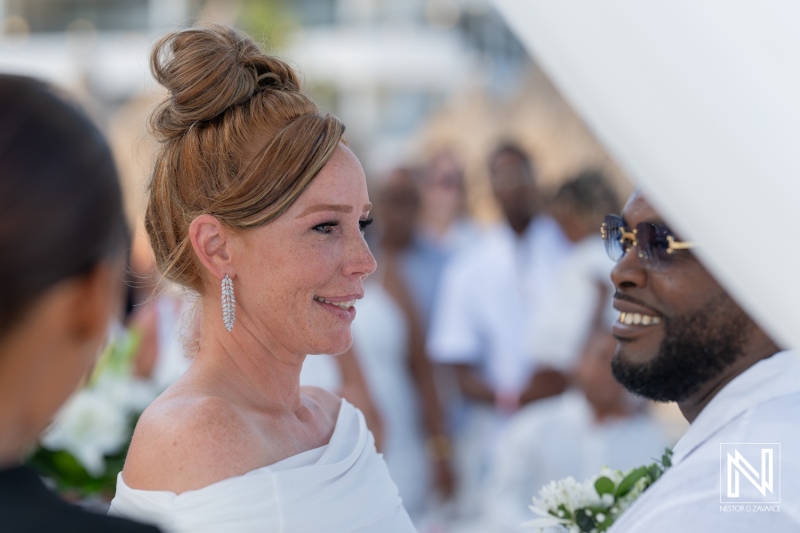 A joyful wedding ceremony taking place on a beach during a sunny afternoon, featuring a bride and groom exchanging vows with guests nearby