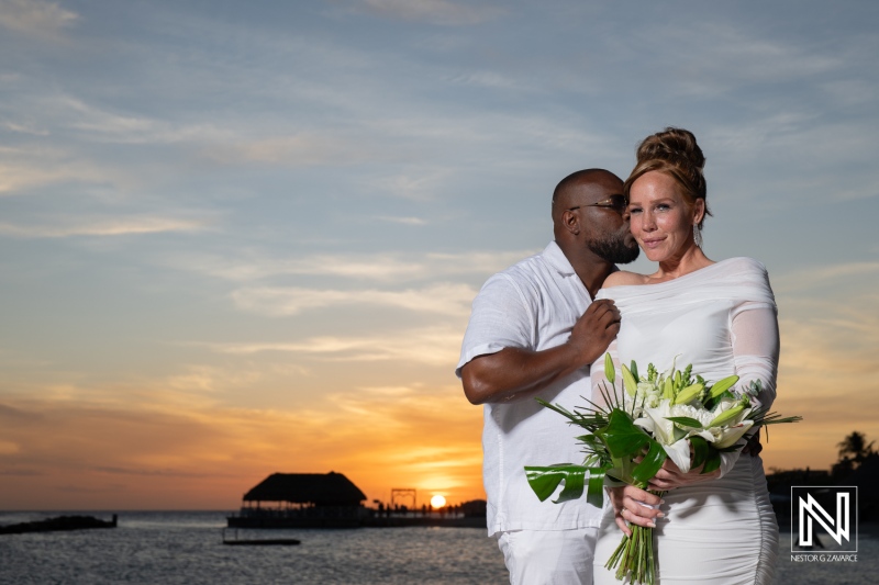 A romantic beach wedding at sunset featuring a couple celebrating their love with flowers in hand on a tropical shore