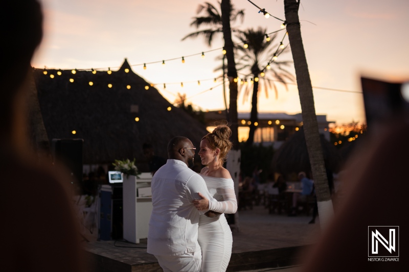 Couple enjoying a romantic dance under string lights at a tropical beach venue during sunset in a picturesque outdoor setting