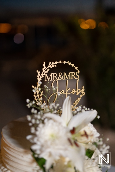 A beautiful wedding cake featuring an elegant topper for Mr and Mrs Jakob, adorned with delicate flowers, captured during a joyful celebration in a lovely venue