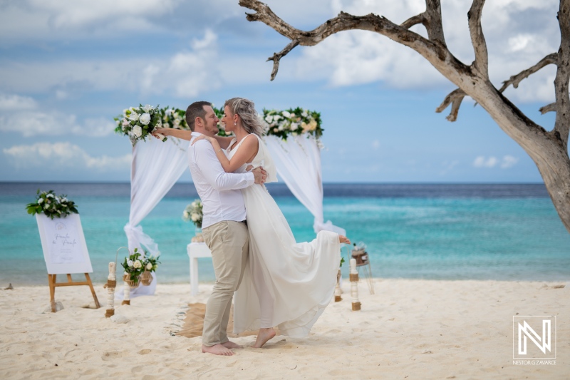 Couple embraces during wedding ceremony at Cas Abao Beach in Curacao with ocean and tree in background