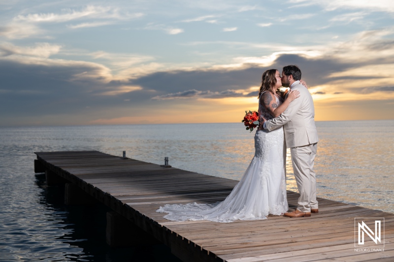 Couple shares a romantic moment at sunset during their wedding at Dreams Curacao Resort on a wooden pier by the sea