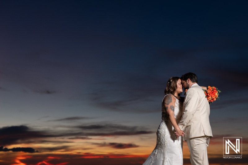 Couple shares a romantic kiss during their wedding ceremony at Dreams Curacao Resort as the sun sets in the background