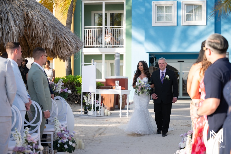 Wedding ceremony at Renaissance Wind Creek Curacao Resort on a beach with guests seated and bride walking with her father