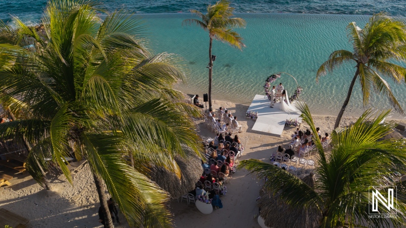 Wedding ceremony at Renaissance Wind Creek Curacao Resort on a beach with guests and palm trees near the sea