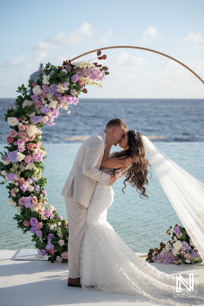 Couples share a kiss during their wedding ceremony at Renaissance Wind Creek Curacao Resort by the ocean under a floral arch