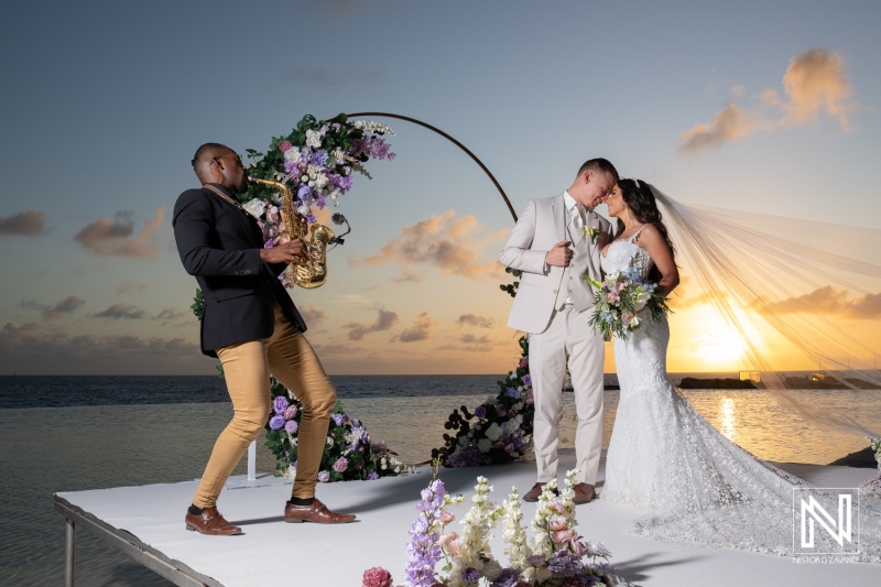 Couple shares a kiss during their wedding at Renaissance Wind Creek Curacao Resort while a saxophonist plays music
