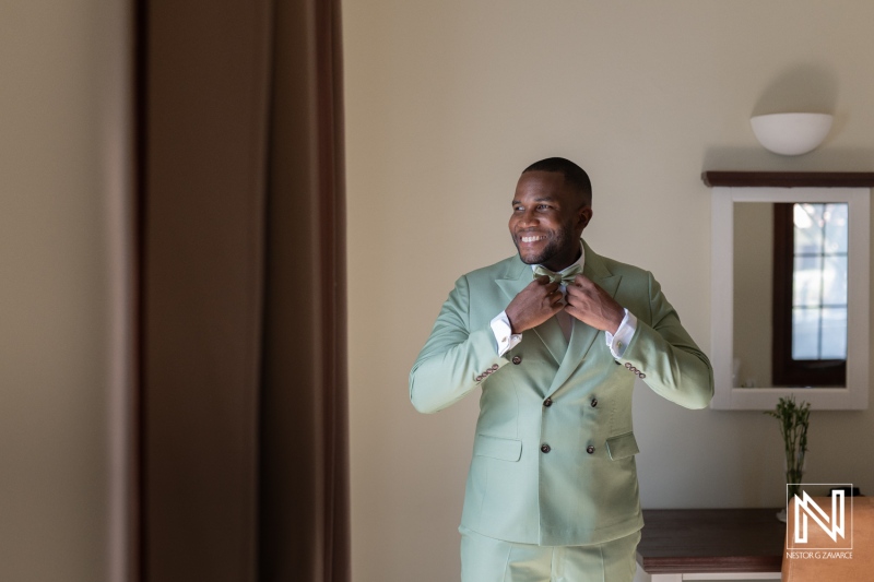 Groom adjusting his bowtie in a bright wedding suite interior before the ceremony in a stylish mint green suit during a joyful morning preparation