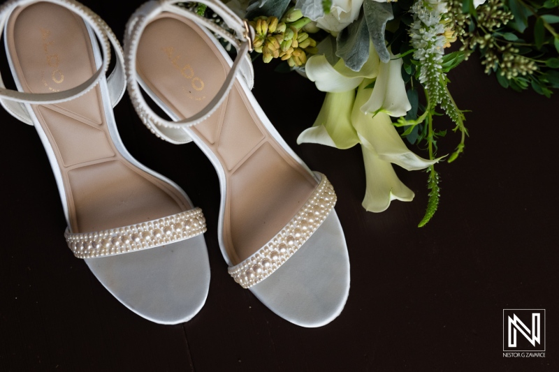 Elegant white sandals adorned with pearls resting beside a bouquet of fresh flowers, ready for a special occasion in a beautifully arranged setting