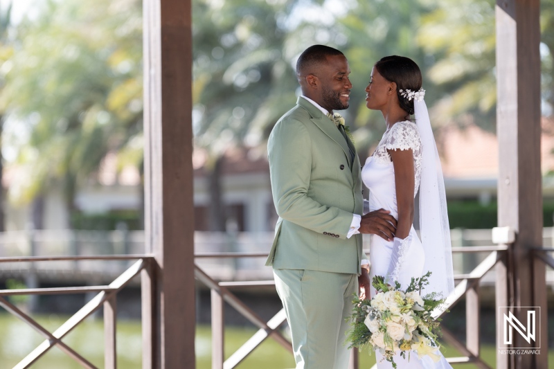 A joyful couple exchanges loving glances during their outdoor wedding ceremony by the serene waterfront in the afternoon light surrounded by lush greenery