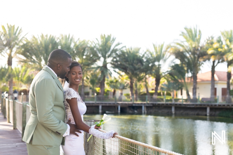 A romantic couple embraces by the serene lake surrounded by palm trees during their wedding celebration in a sunny outdoor venue