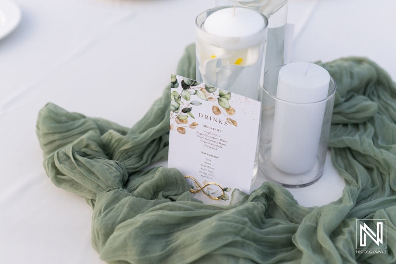 Elegant table setting with a drink menu and decorative candles at a wedding reception in a garden during the afternoon