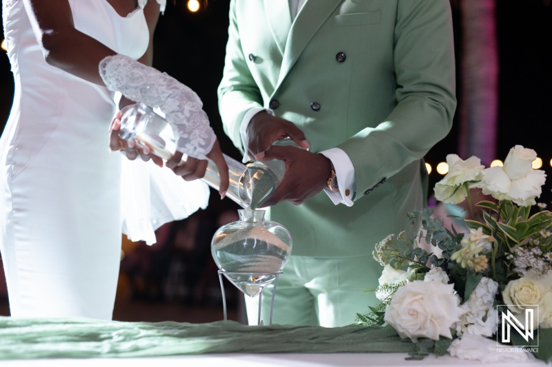 Elegant couple pours water together during a wedding ceremony outdoor at night, surrounded by flowers and soft lights, celebrating their love with a unity ritual