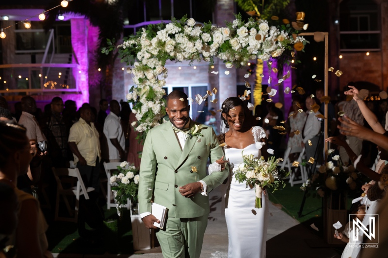 Young couple joyfully exits their wedding ceremony surrounded by friends and family in a beautifully decorated outdoor venue during an evening celebration