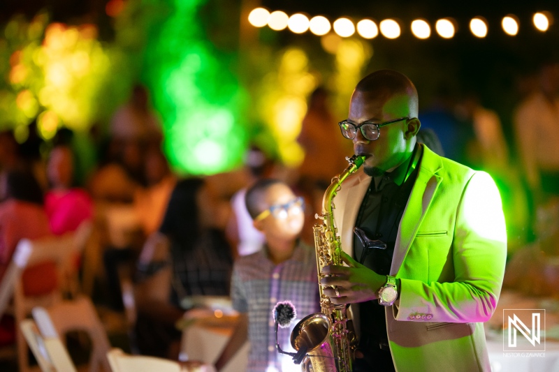 Saxophonist performs passionately at an outdoor evening event with vibrant lighting and an engaged audience in the background