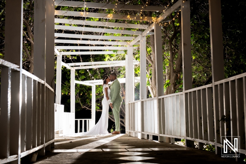 Romantic couple embraces on a beautifully lit walkway in an outdoor wedding setting at night surrounded by greenery and soft lights