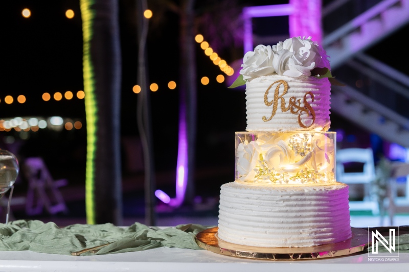 Elegant three-tier wedding cake displayed at a nighttime outdoor reception with soft lighting and floral accents