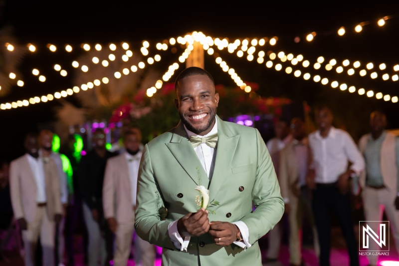 A groom smiling joyfully at a vibrant wedding reception surrounded by festive lights and guests in elegant attire during nighttime celebration