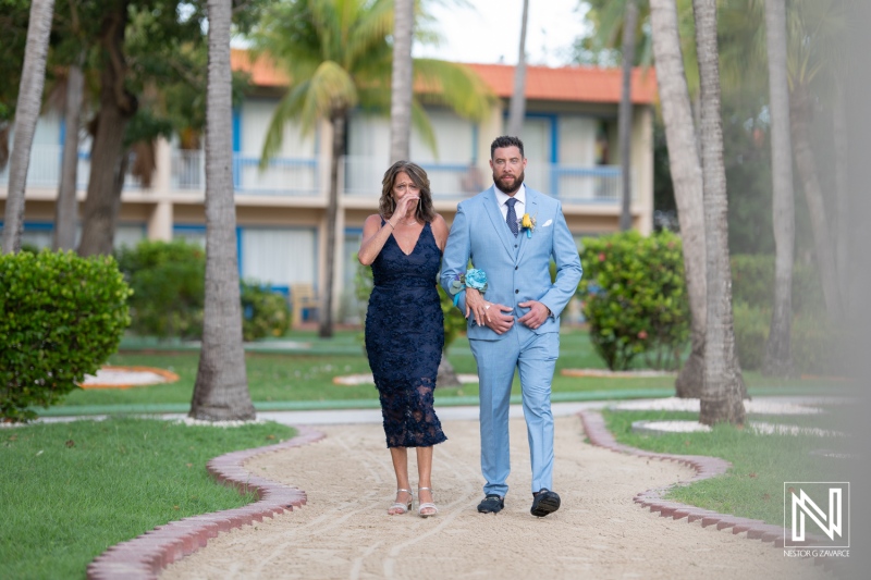 Wedding ceremony at Sunscape Curacao Resort with a joyful mother and groom walking down a sandy path surrounded by tropical palm trees