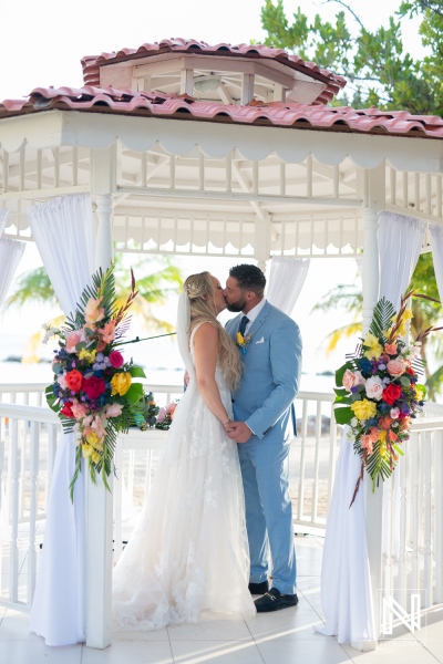 Couple exchanges vows in enchanting outdoor ceremony at Sunscape Curacao Resort amidst vibrant floral arrangements and stunning ocean backdrop