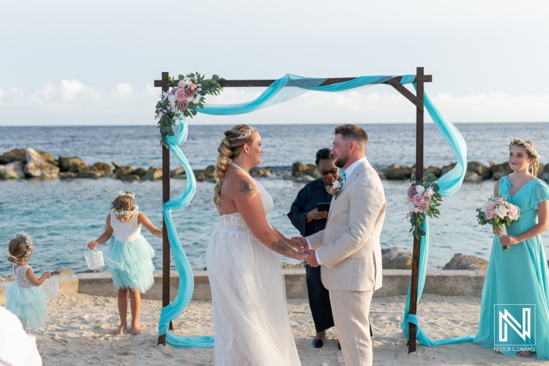 A Couple Exchanges Vows During a Romantic Beach Wedding Ceremony at Sunset, Surrounded by Friends and Family in Festive Attire on a Sandy Shoreline