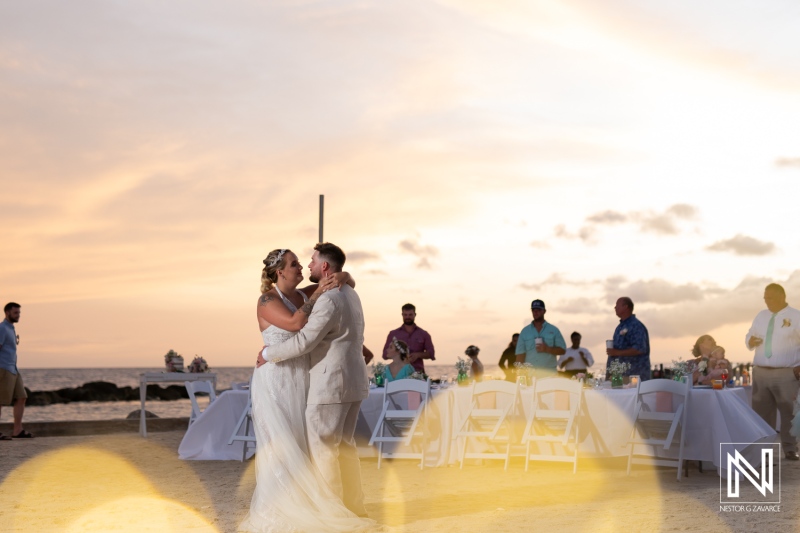 Couple Shares a Romantic First Dance on a Beach During Sunset, Surrounded by Guests Celebrating Their Wedding in a Picturesque Coastal Setting