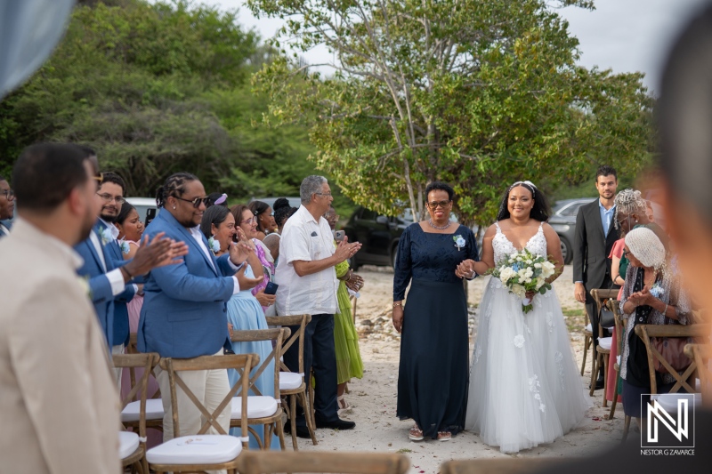 Wedding celebration at Playa Hunku in Curacao featuring a bride walking down the aisle with her mother surrounded by guests