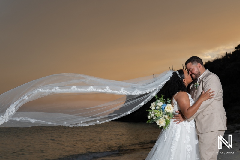 Couple shares a romantic moment during their wedding ceremony at Playa Hunku in Curacao at sunset with flowing veil and floral bouquet