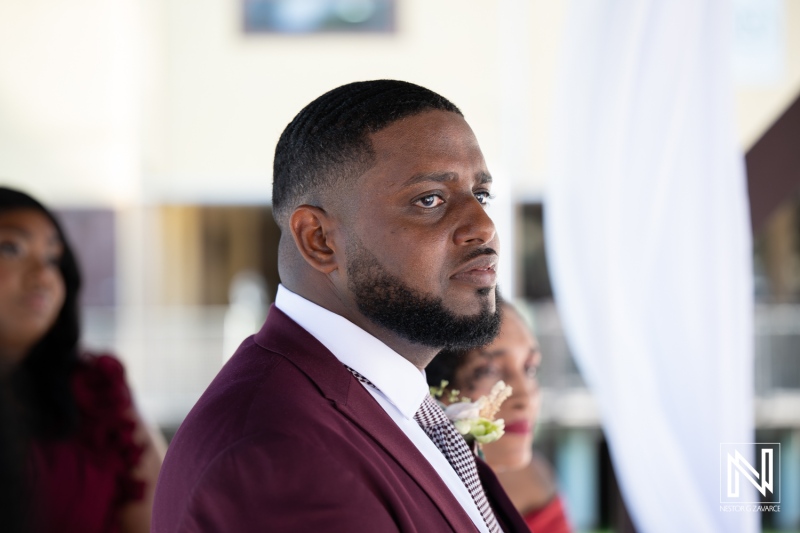 Groom in formal attire observes wedding ceremony at Acoya Curacao Resort with lovely setting in the background