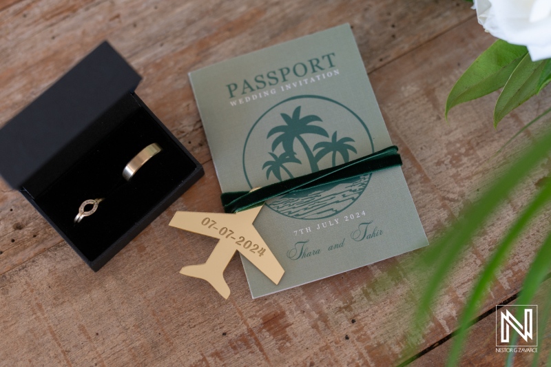 A Stylish Wedding Invitation Alongside a Decorative Ring Box and a Wooden Plane Tag, All Arranged on a Wooden Surface With a Floral Centerpiece