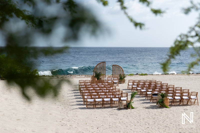 A Serene Beachfront Wedding Setup at a Tropical Location With Carefully Arranged Chairs and a Decorative Arch Facing the Ocean Under a Bright Sky