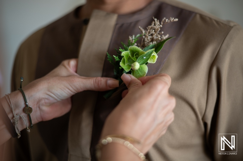 A Close-Up of a Person Attaching a Floral Boutonniere to a Man\'s Shirt at a Wedding Preparation in a Softly Lit Room, Showcasing Attention to Detail and Personal Touches