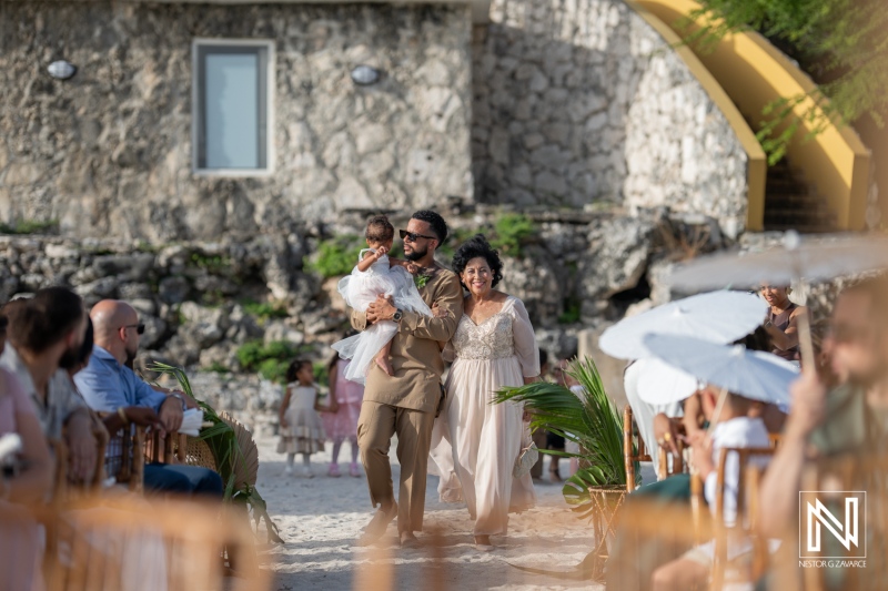 A Family Walks Down a Sandy Beach Aisle During a Wedding Ceremony Surrounded by Guests in a Coastal Setting