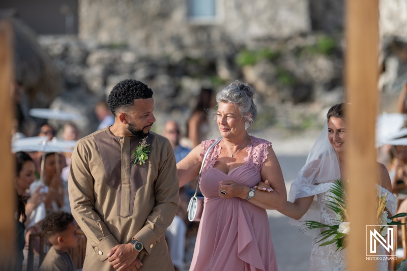 A Joyful Wedding Ceremony on a Beach With a Groom Eagerly Awaiting His Bride Alongside Her Mother and Guests