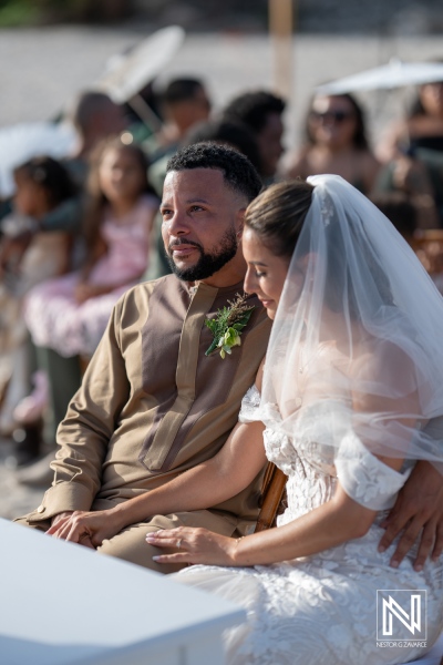 Couple Sitting Together During a Beach Wedding Ceremony, Surrounded by Guests in a Beautiful Outdoor Setting on a Sunny Day