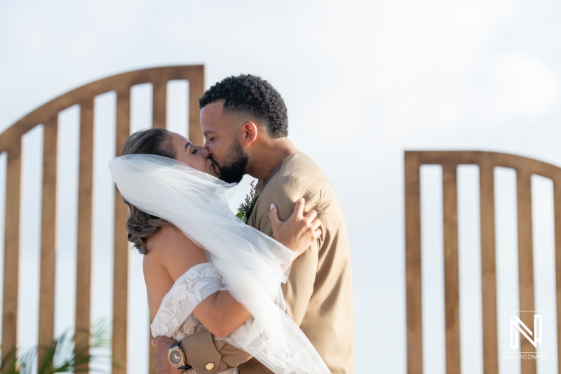 A Joyful Couple Shares a Loving Kiss During an Outdoor Wedding Ceremony at a Beachside Venue Under a Clear Sky in the Afternoon