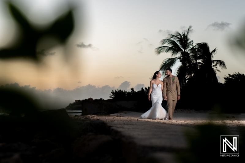 A Couple Walks Hand in Hand Along a Tropical Beach at Sunset, Surrounded by Palm Trees, Celebrating Their Romantic Wedding Moment