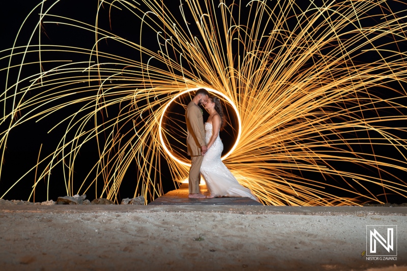 A Romantic Couple Poses on the Beach at Night While Sparks From Steel Wool Create a Stunning Light Display Around Them, Showcasing the Beauty of Love and Celebration