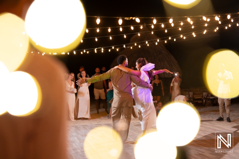 A Joyful Couple Dances Under Fairy Lights at a Beachside Celebration During a Summer Evening, Surrounded by Family and Friends Enjoying the Magical Atmosphere