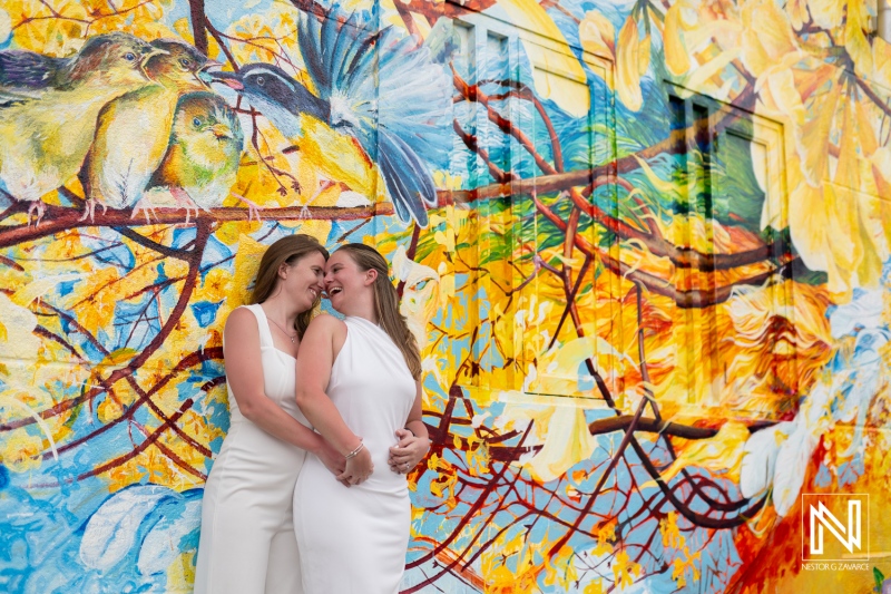 LGBT wedding celebration at sunset in Willemstad, Curacao featuring a colorful mural backdrop and joyful moments between two brides