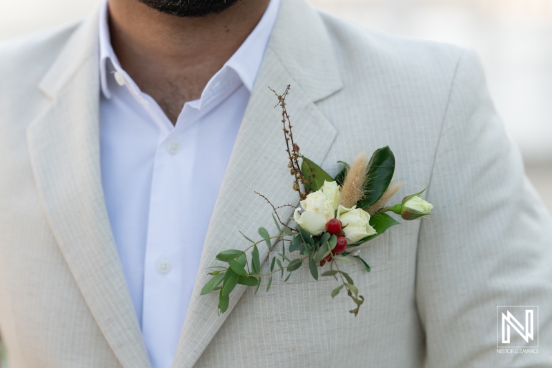 Elegant groom wearing a light-colored suit with a floral boutonniere during an outdoor wedding ceremony in a scenic location at sunset