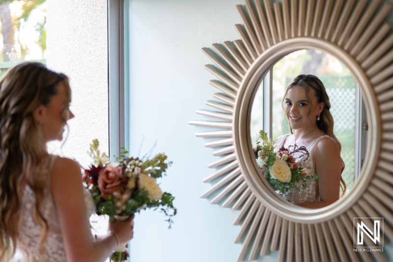 A bride admires her reflection in a round mirror while holding a beautiful bouquet inside a bright room before the wedding ceremony