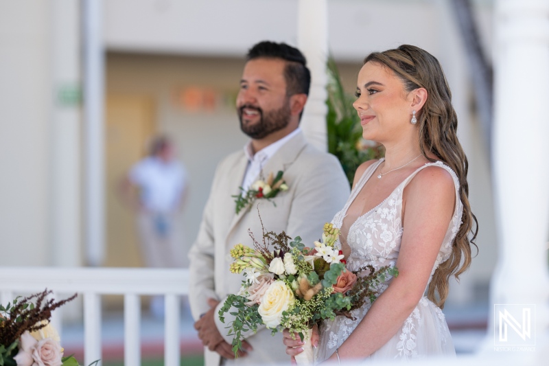 A couple exchanges vows during an outdoor wedding ceremony in a beautiful garden setting under bright daylight surrounded by family and friends