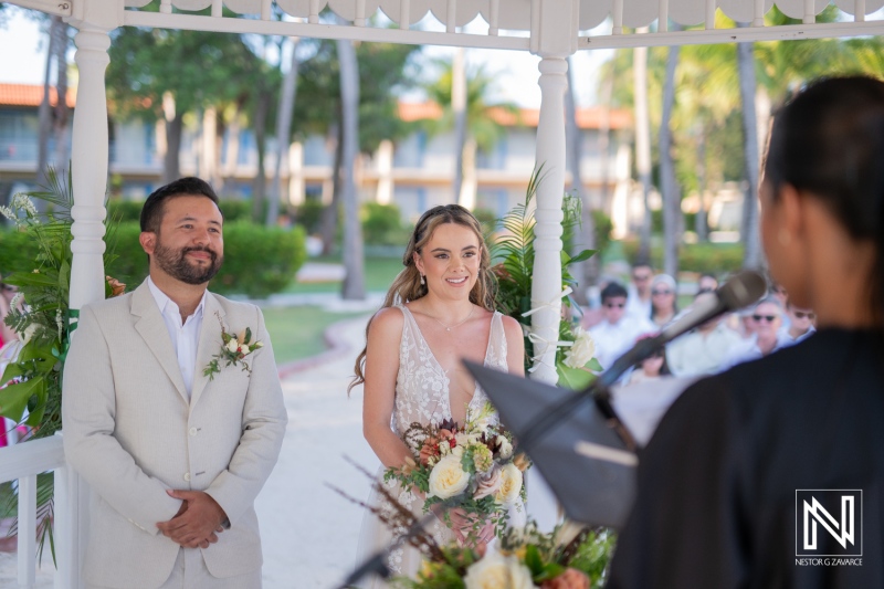 Romantic outdoor wedding ceremony under a gazebo with guests witnessing heartfelt vows exchanged at a tropical resort in the afternoon sunshine