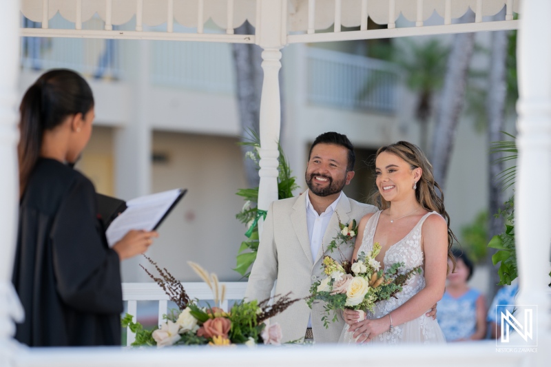 Romantic outdoor wedding ceremony with a smiling couple under a gazebo in a tropical setting during daytime