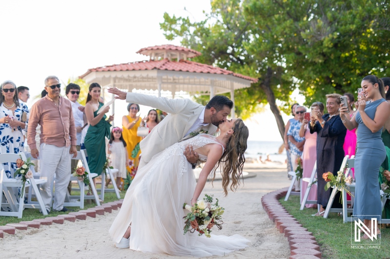 A joyful couple celebrates their wedding with a romantic kiss during an outdoor ceremony by the beach in a beautiful garden setting