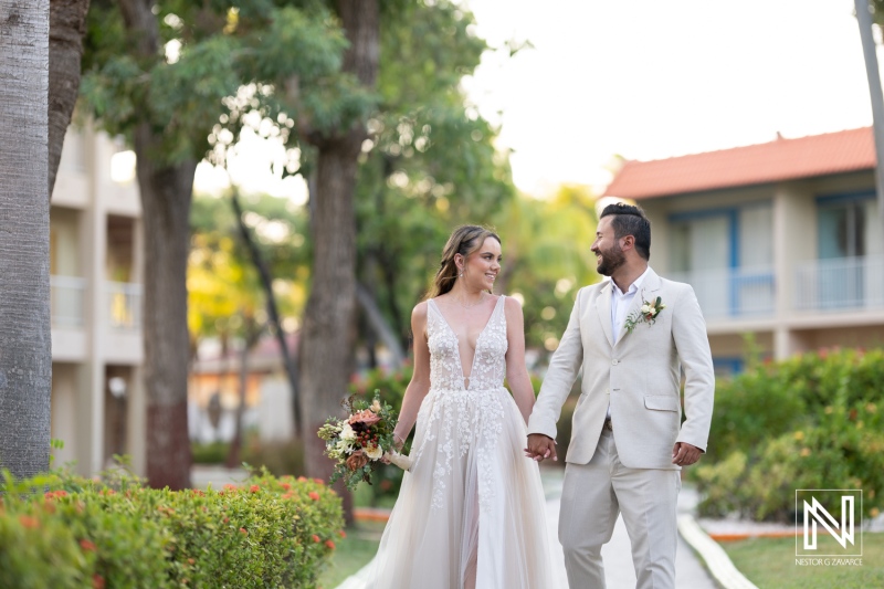 Newlyweds walking hand in hand through a lush garden at sunset after their outdoor wedding ceremony near a colorful resort