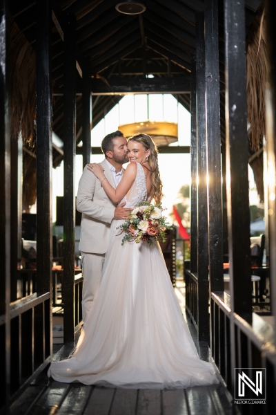 A couple in elegant wedding attire embraces on a decorative wooden walkway illuminated by soft light on a beautiful day at a romantic venue