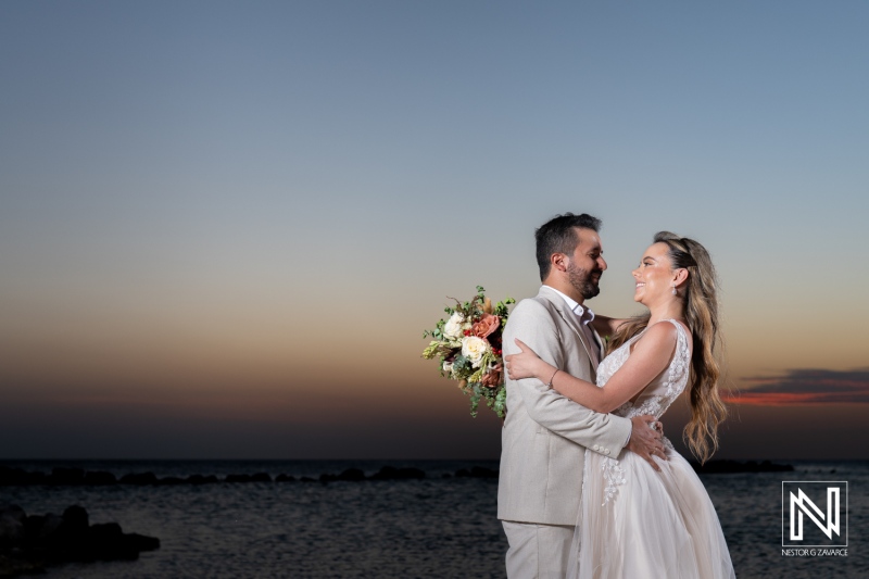 Bride and groom celebrating their wedding by the sea at sunset, capturing a joyful moment on a beautiful evening